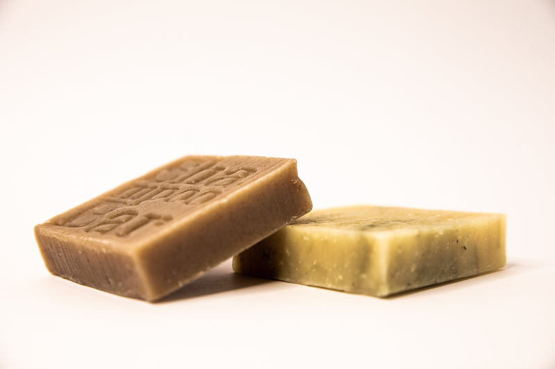 Close up of both types of shampoo bars, one for curly hair and one for fine hair, lying down on a white background