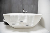 image of white cotton towel set over side of white freestanding oval bath with navy and white striped bag partially visible at rear.