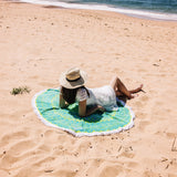 Lady in a white dress with a straw hat lying on blue and green organic mandala towel at the beach