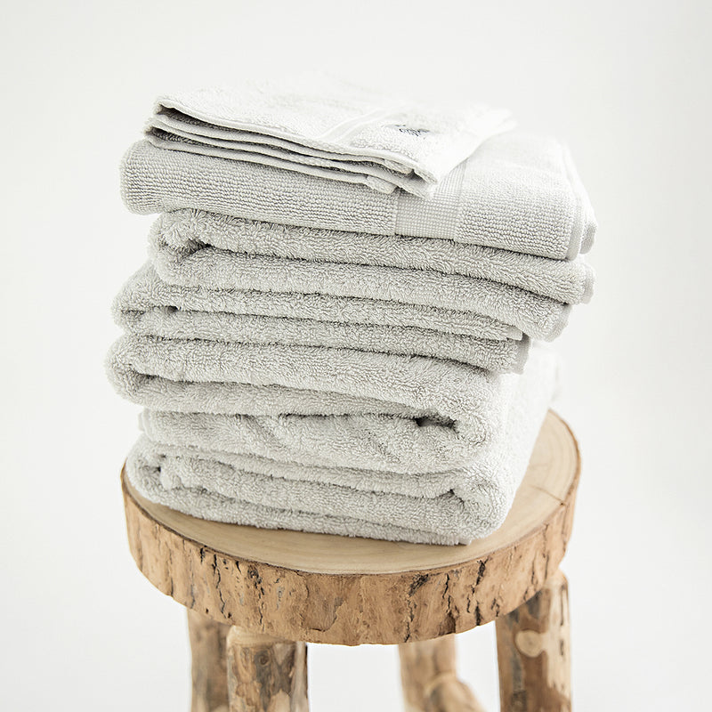 7 piece organic towel set in 700GSM Stone. 2 bath towels, 2 hand towels, 2 face towels and one bath mat. Stacked on a stool.