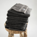 7 piece organic towel set in 700GSM charcoal. 2 bath towels, 2 hand towels, 2 face towels and one bath mat. Stacked on stool.