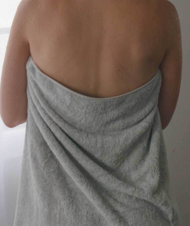 Image of lady with organic cotton towel draped around her in stone. View is from the back and shows folds and texture of towel.