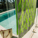 Close up of green and grey towel over glass fencing around a pool with bag beside.