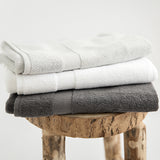 Organic cotton bath mats in stone, white and charcoal, folded on stool.