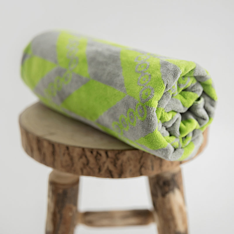 Organic beach towel rolled up on stool. Herringbone print in green and grey.
