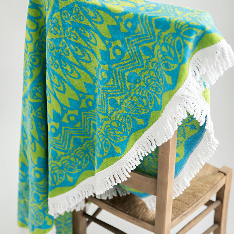 Organic mandala towel, round 130cm draped across back of chair. Green and blue with white tassel