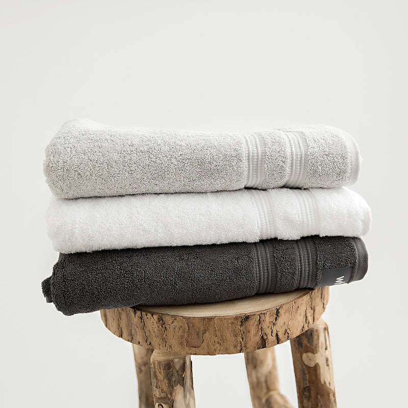 Organic bath towels in 700GSM GOTS cotton. Pictured in stone, white and charcoal.