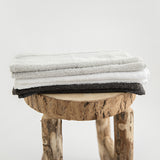 Organic cotton face towels folded on stool. Stone, white and charcoal.