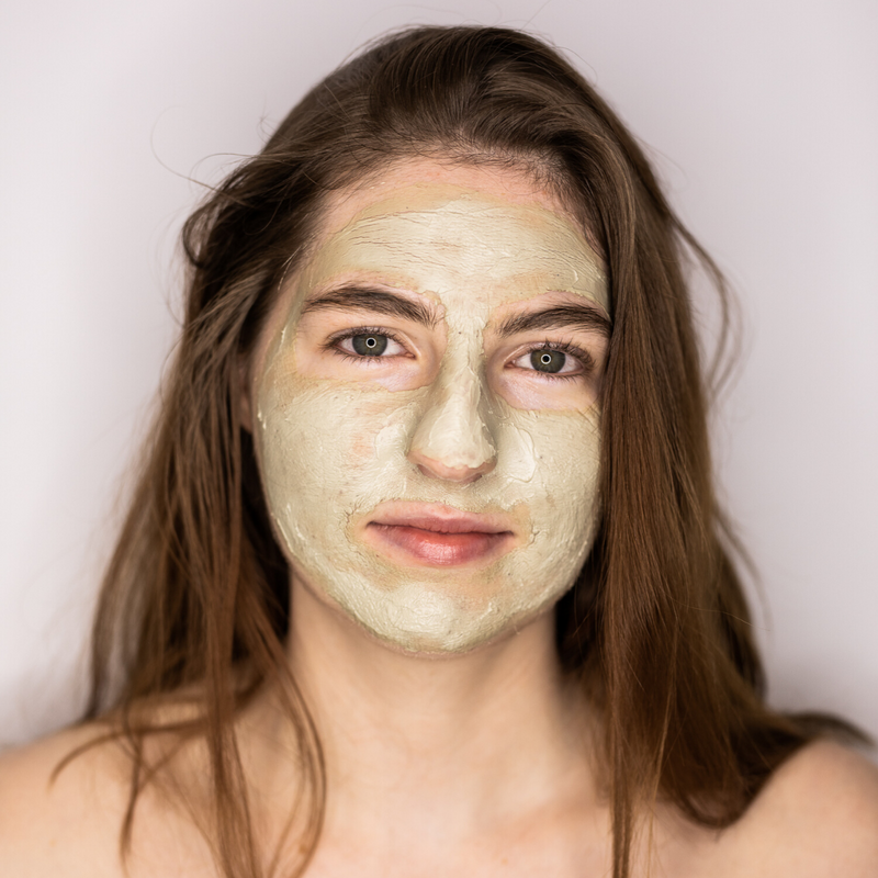 Woman with long brown hair wearing soft clay mask on her face